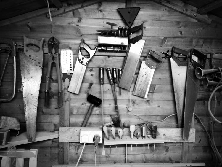 Black and white photo of vintage hand tools hanging neatly on a wooden workshop wall.